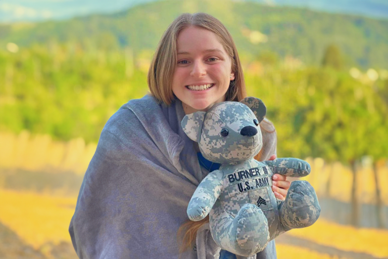 a young woman holds a stuffed Teddy bear with the words "Burner III U.S. Army" on it