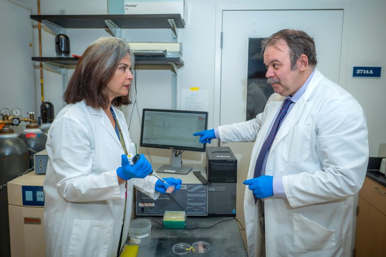 Man and woman in white lab coats talk in front of computer