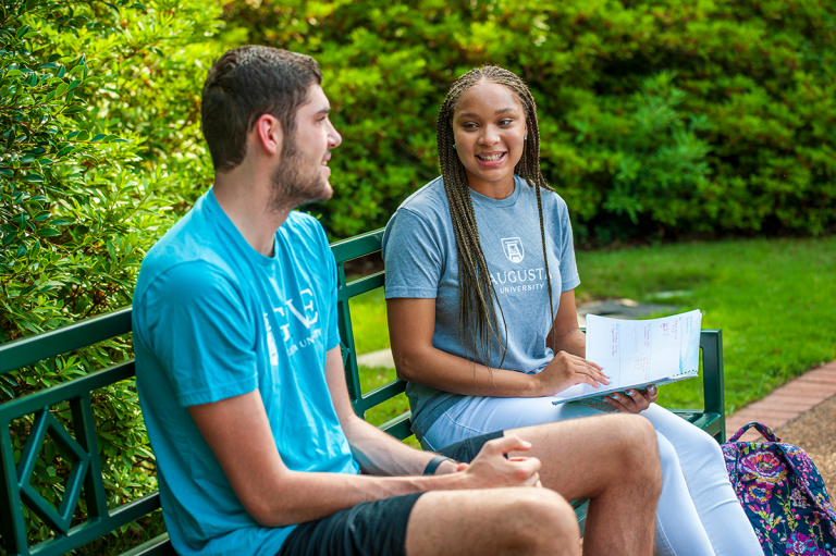 Two students sitting on a bench along Augusta University's History Walk on the Summerville Campus.