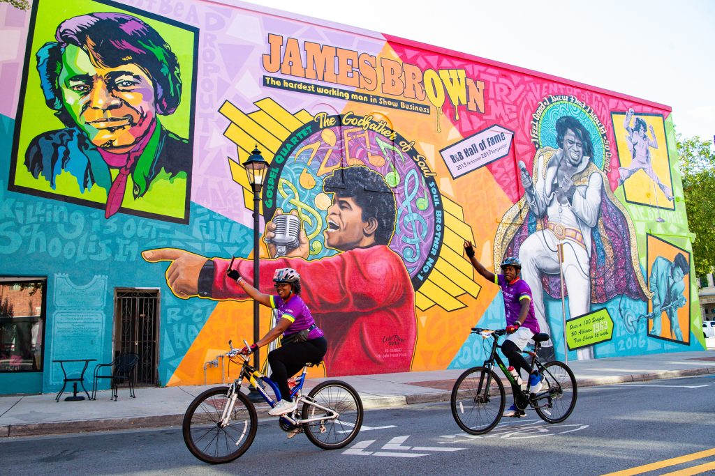 Two bikers pedal past James Brown mural in downtown Augusta.