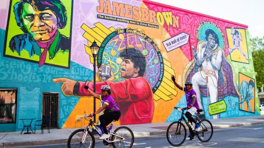 Two bikers pedal past James Brown mural in downtown Augusta.