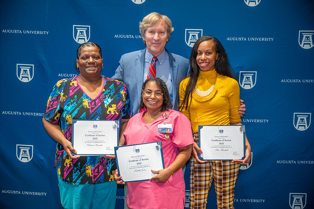 Three women hold certificates while standing with a man for a photo.