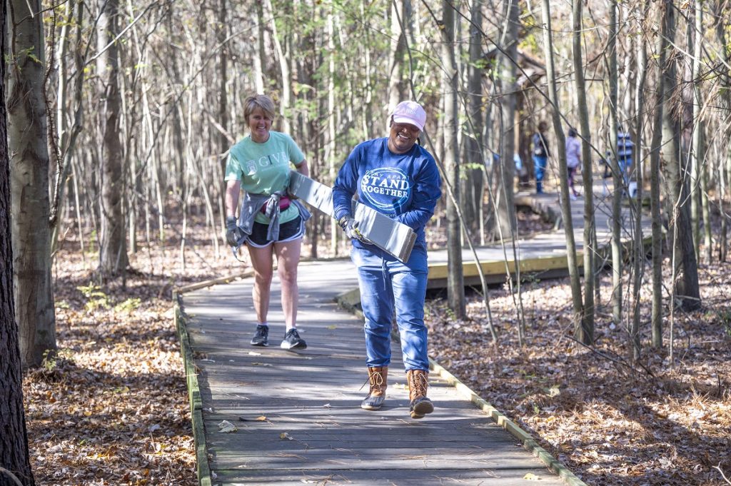 Two ladies carry a plank to help rebuild a boardwalk