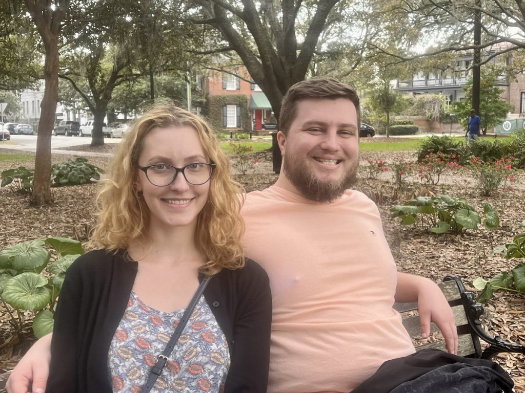 man and woman sit on a park bench smiling
