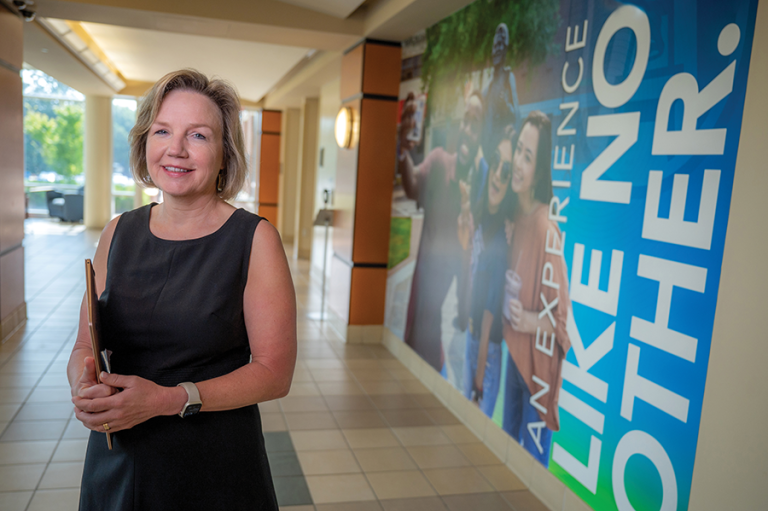 woman holding a folder stands in front of a wall mural featuring two students next to the words "An experience like no other."