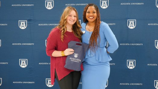 A high school student holds the early acceptance bag given to her by Augusta University while taking a photo with a representative of Augusta University