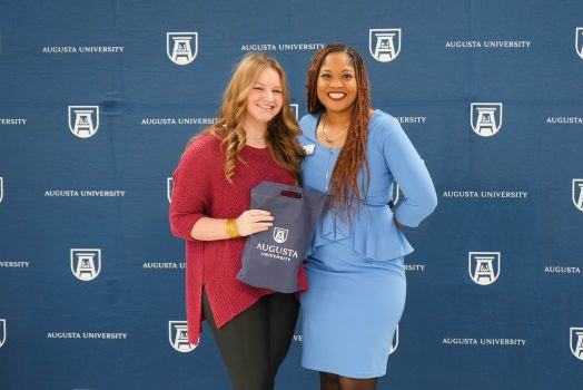 A high school student holds the early acceptance bag given to her by Augusta University while taking a photo with a representative of Augusta University