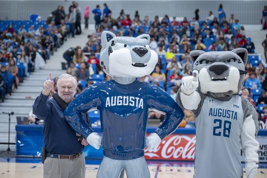 Man and mascot standing next to a statue