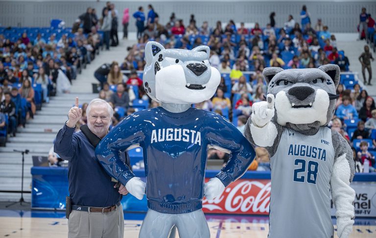 Man and mascot standing next to a statue