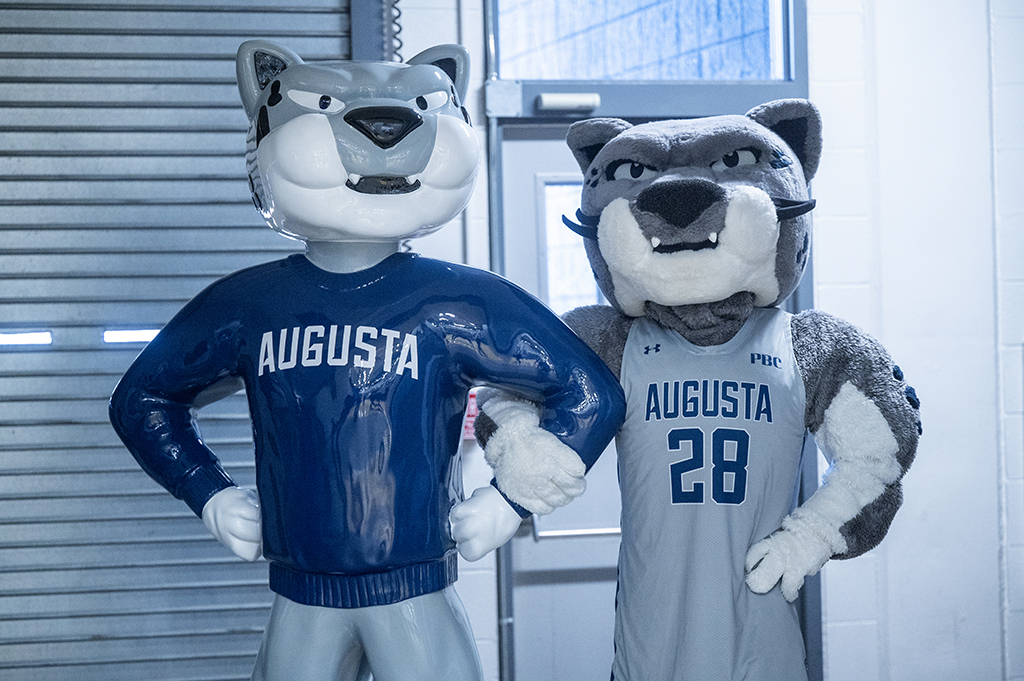An athletics mascot posing with a statue.