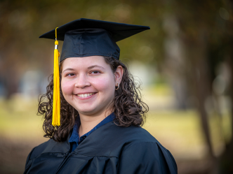 woman wearing a graduation cap and gown smiling outside