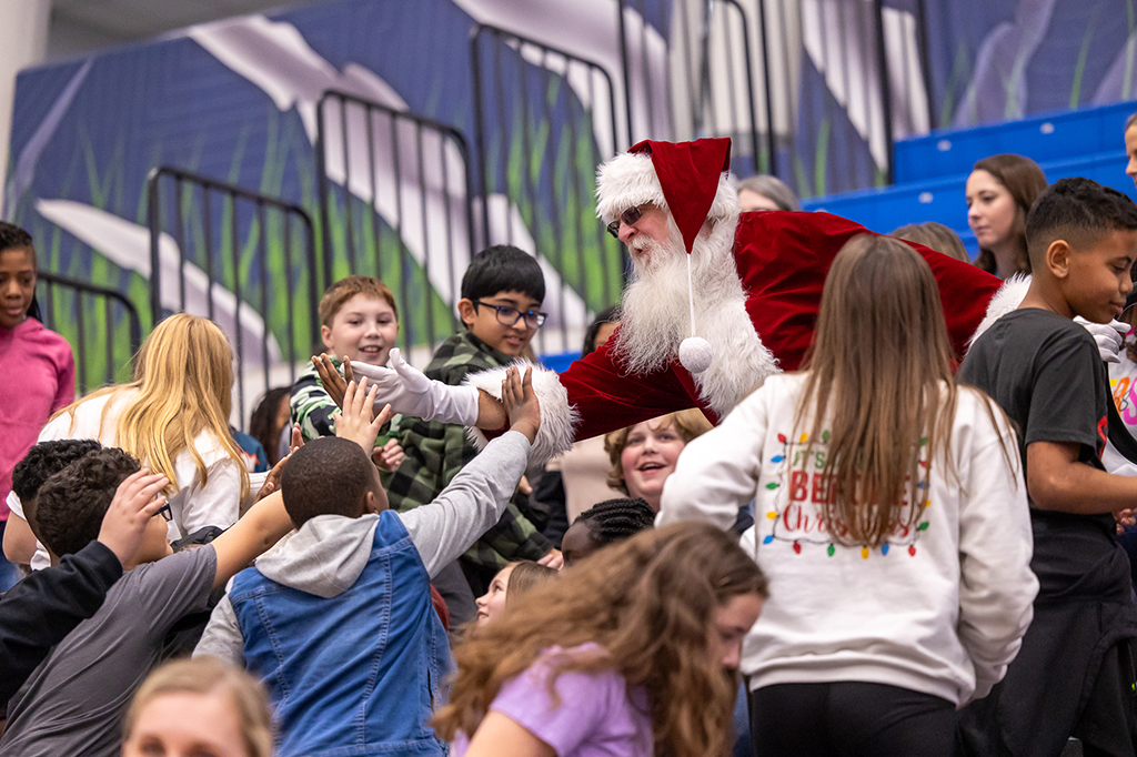 Santa Claus greets children, giving several high fives.