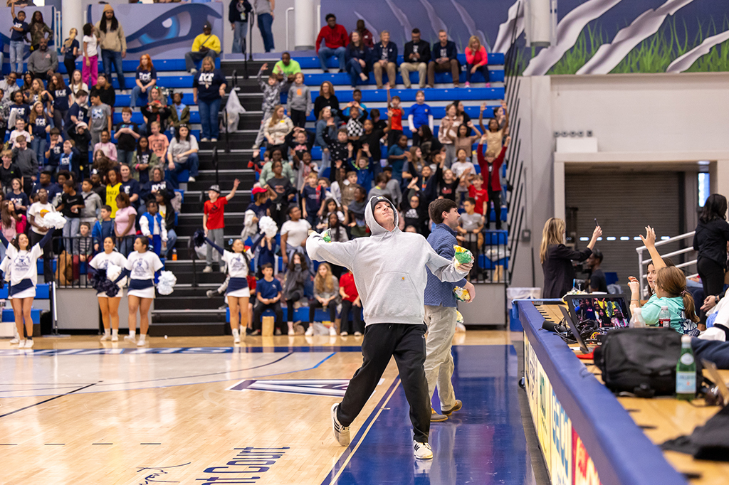 A male college student throws soft toys into the stands at a basketball game.