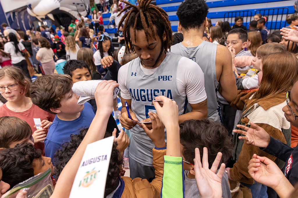 A college basketball player signs autographs for kids.
