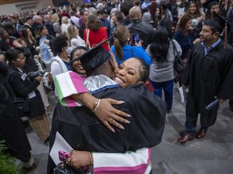 an undergraduate hugs a family member with a crowd of people around them inside the Convention Center at the Augusta Marriott after the graduation ceremony
