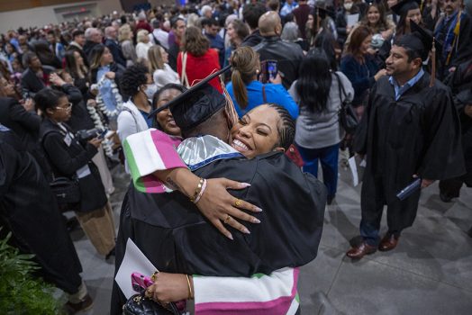 an undergraduate hugs a family member with a crowd of people around them inside the Convention Center at the Augusta Marriott after the graduation ceremony