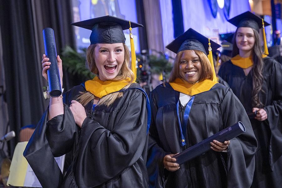 Three young women in graduation caps and gowns celebrate having graduated from their master's programs.