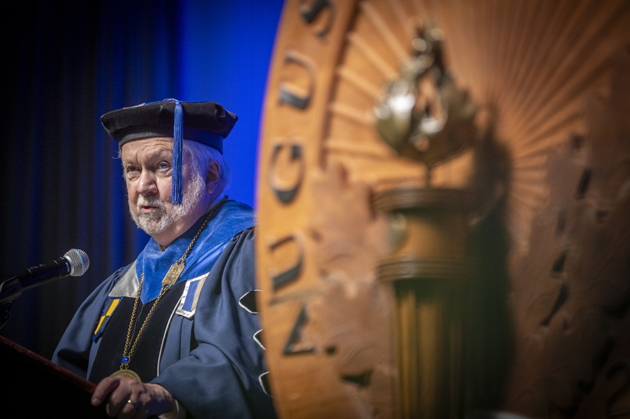A man stands at a podium and delivers a speech while wearing a graduation cap and gown.