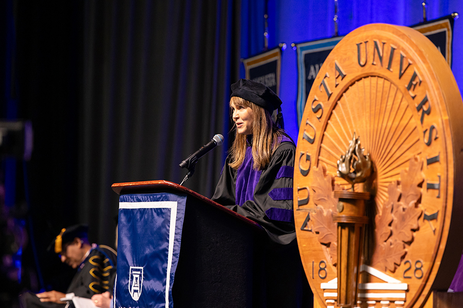 A woman in graduation cap and gown stands at a podium to give a speech.