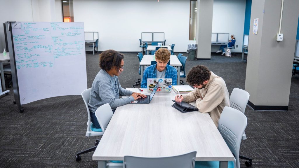 Three students work at table in a library.