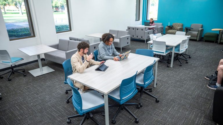 Two students read iPads at table in library.