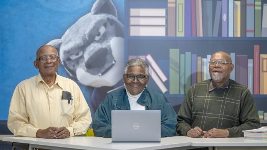 Two men and a woman pose for a photo with a computer in front of them