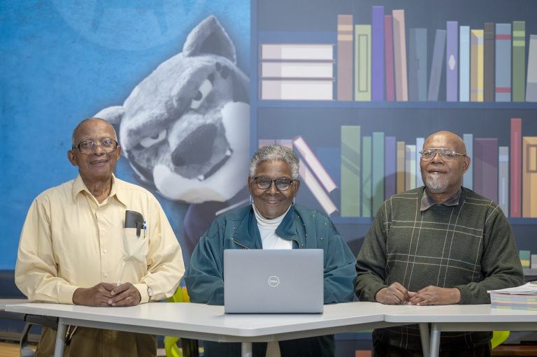 Two men and a woman pose for a photo with a computer in front of them