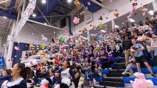 Students and cheerleaders throw stuffed animals onto a basketball court