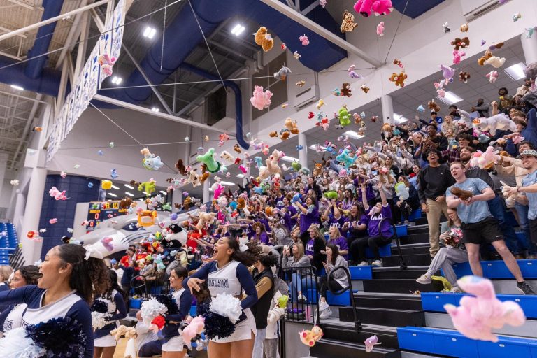 Students and cheerleaders throw stuffed animals onto a basketball court