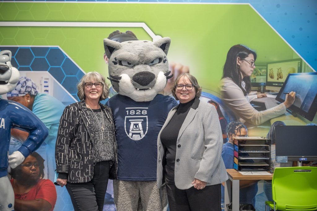 A college mascot that represents a jaguar stands with two women.