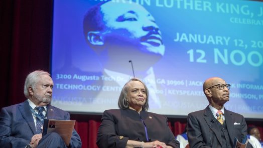 Two men and a woman sit on a stage during a Dr. Martin Luther King Jr. celebration