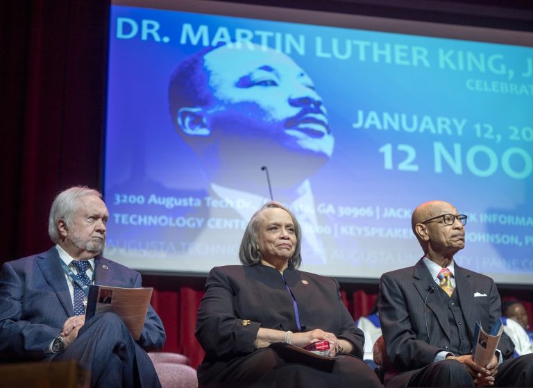 Two men and a woman sit on a stage during a Dr. Martin Luther King Jr. celebration