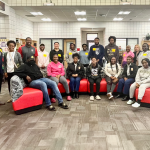 A group of students and teachers and administrators pose for a photo on and around a couch inside a school library