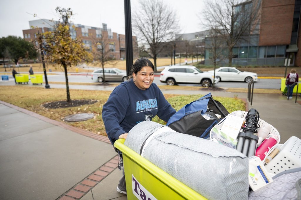 A smiling young lady moves a bin for her dorm room