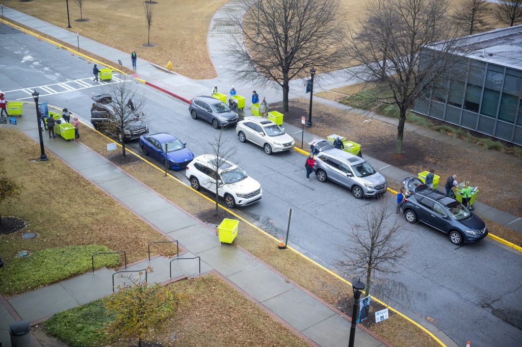 an overhead shot of cars lined up on the street with people moving things into bins for dorm rooms