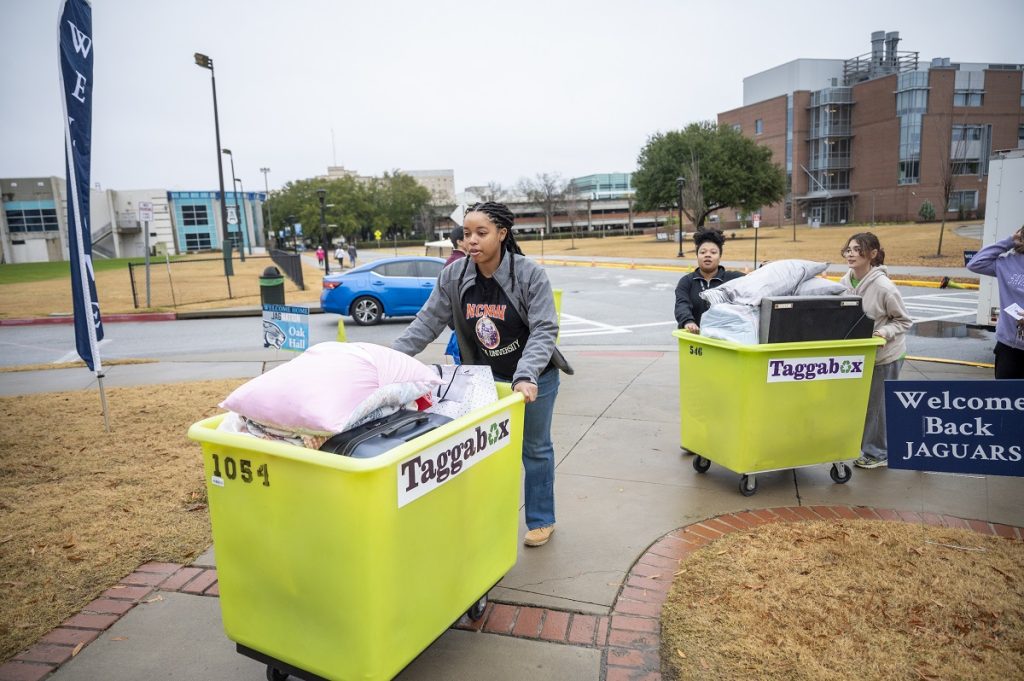 A young lady pushes a bin filled with dorm items
