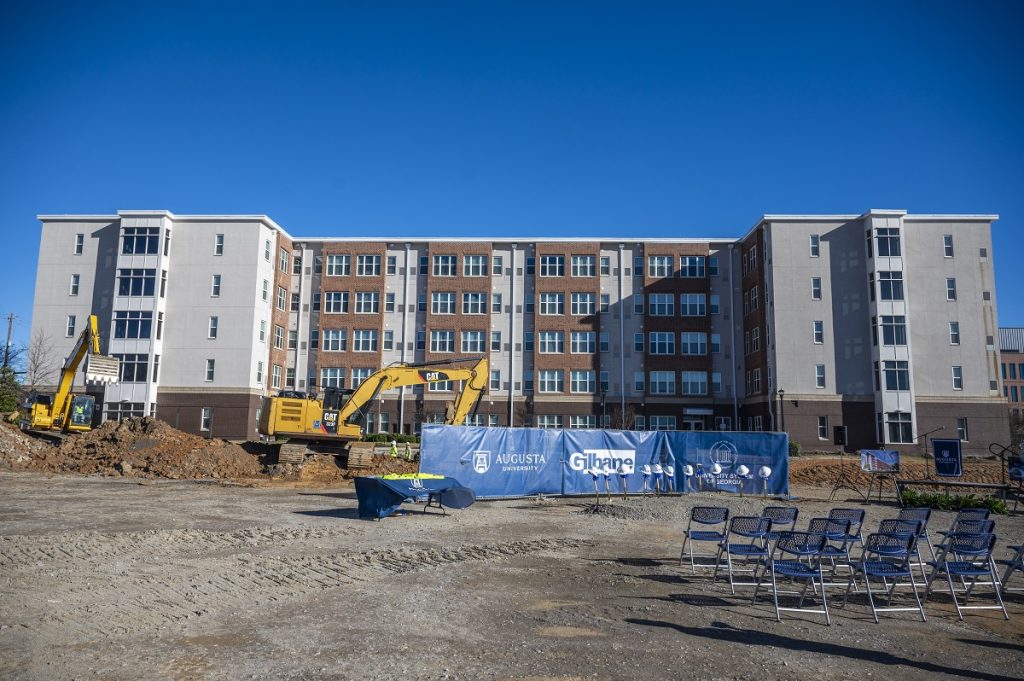 A dorm with an excavator in the foreground at a groundbreaking ceremony