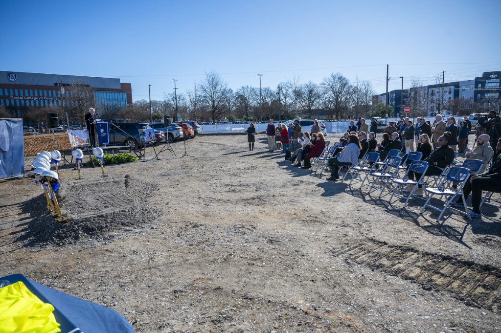 People sitting outside listen to a man speaking at a groundbreaking ceremony at Augusta University
