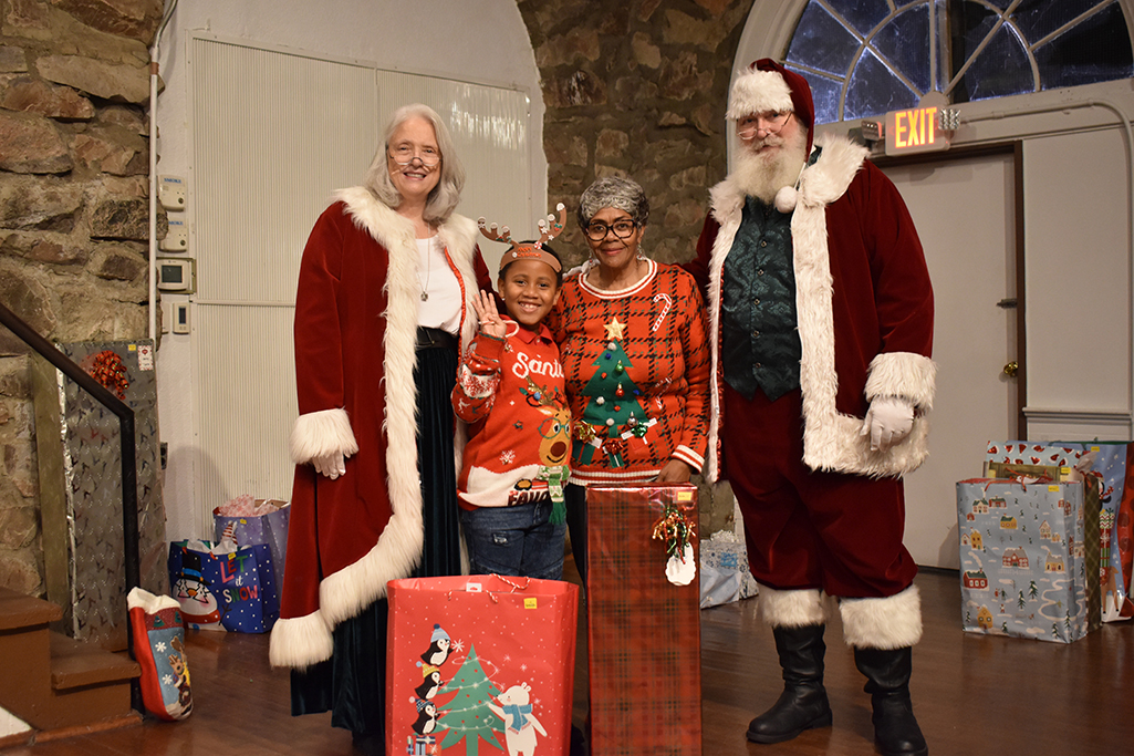 Santa and Mrs. Clause stand with a grandma and her granddaughter behind a couple of presents