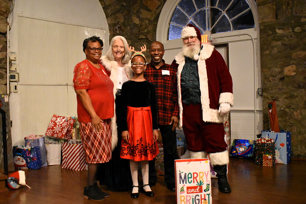 Santa and Mrs. Claus pose for a photo with a grandma, grandpa and granddaughter with a reindeer antler headband, all dressed in Christmas attire