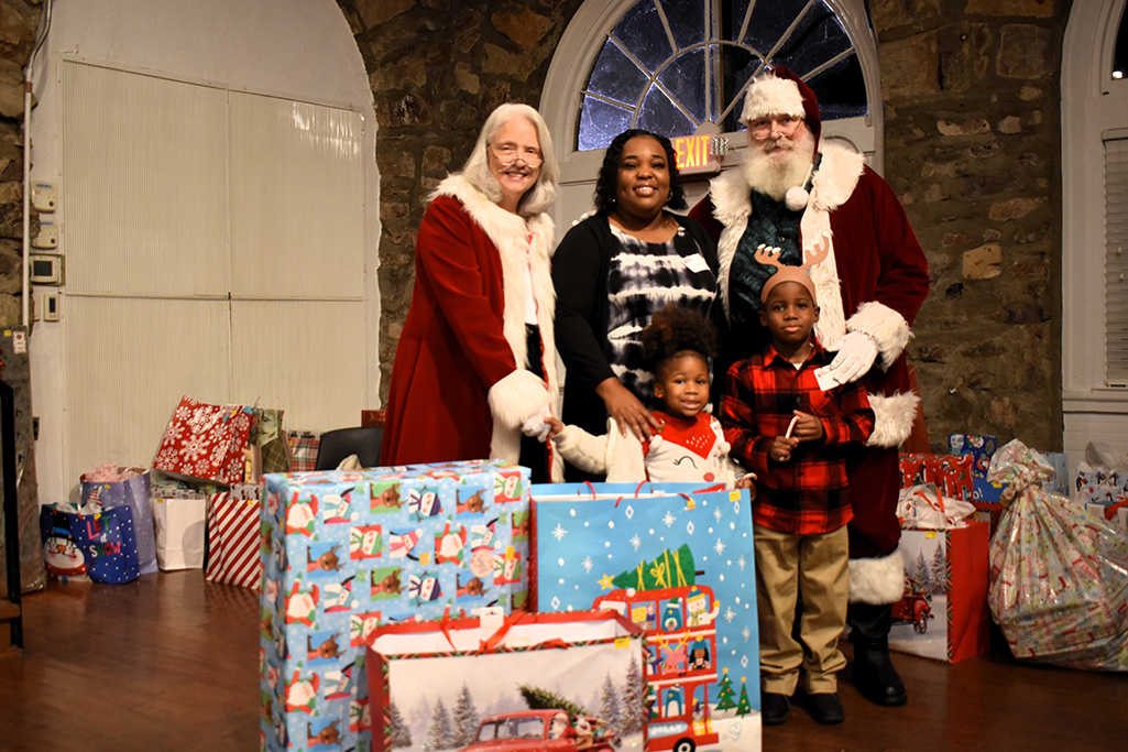 Santa and Mrs. Claus pose with a grandma and her two grandchildren behind presents 