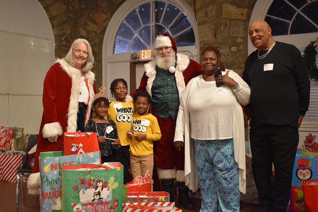 Santa and Mrs. Claus pose with a grandma and grandpa and their three grandchildren surrounded by presents