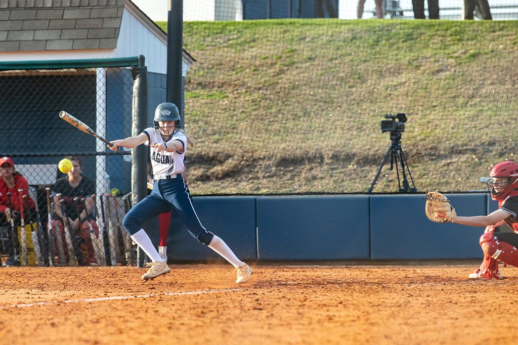 A softball player runs after swinging a bat and making contact with the ball.
