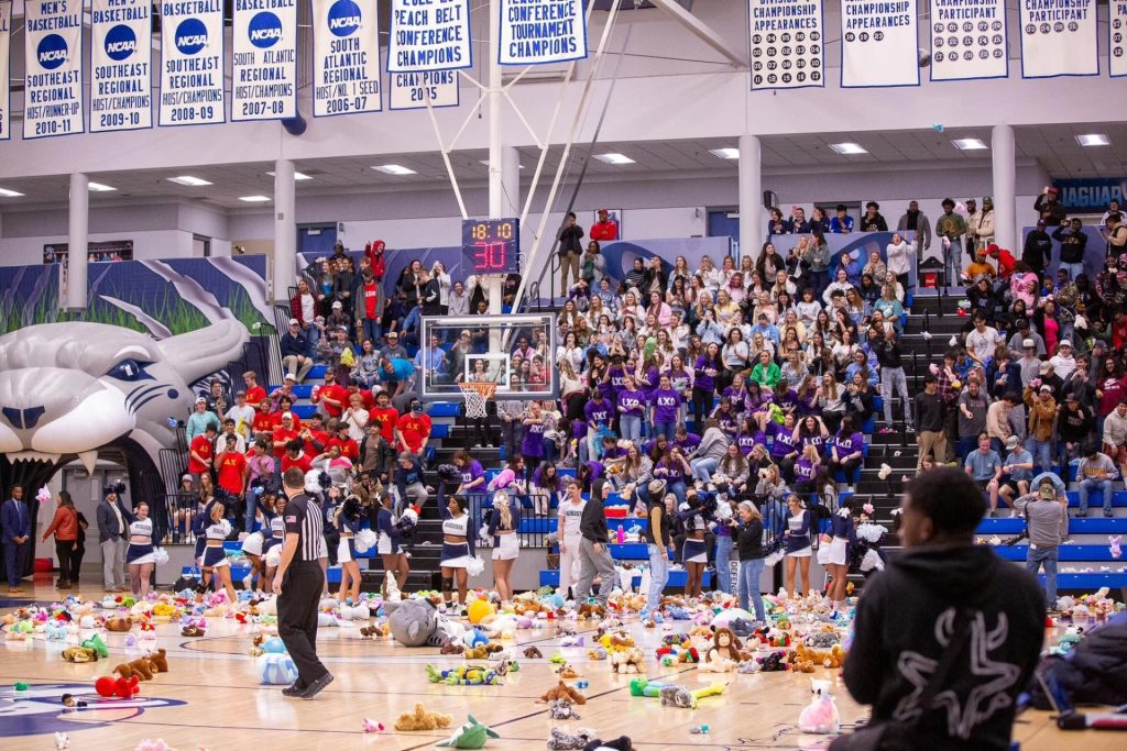 Students at a basketball game throw stuffed animals onto the court with a referee looking on