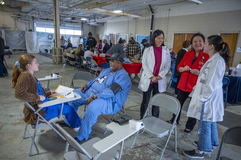 truck drivers sit at various stations with students and nurses and College of Nursing faculty members help them