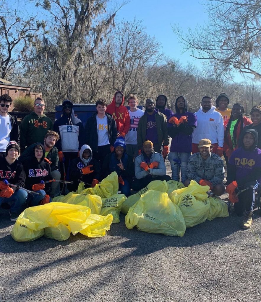 Twenty-one college students in sweatshirts and jackets pose in two rows behind 10 yellow bags of trash after helping with a community service project