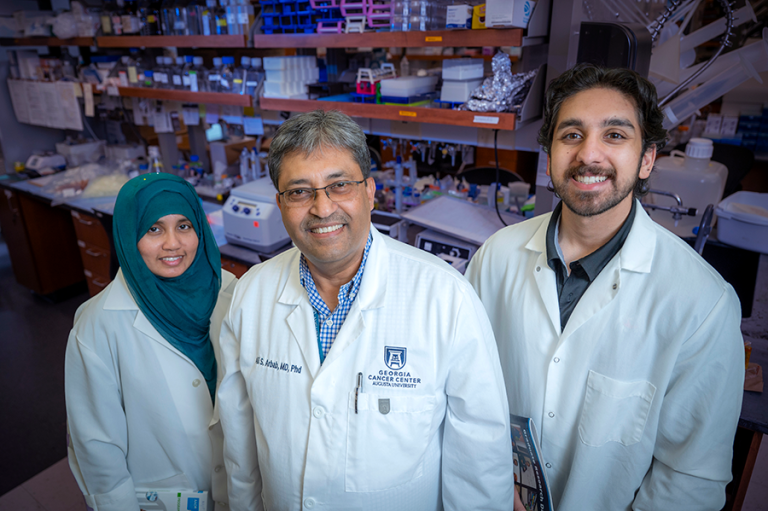 Two men and a woman, all wearing lab coats, stand in a science lab and smile for a photo.