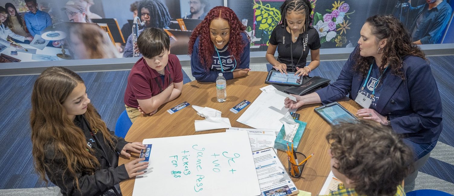 Four students sit around a table with two women from Augusta University in the Augusta University storefront at the Junior Achievement Discovery Center.