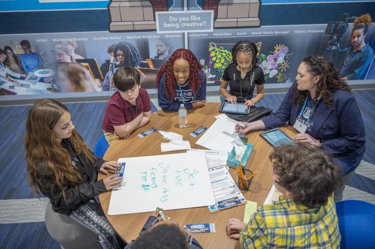 Four students sit around a table with two women from Augusta University in the Augusta University storefront at the Junior Achievement Discovery Center.