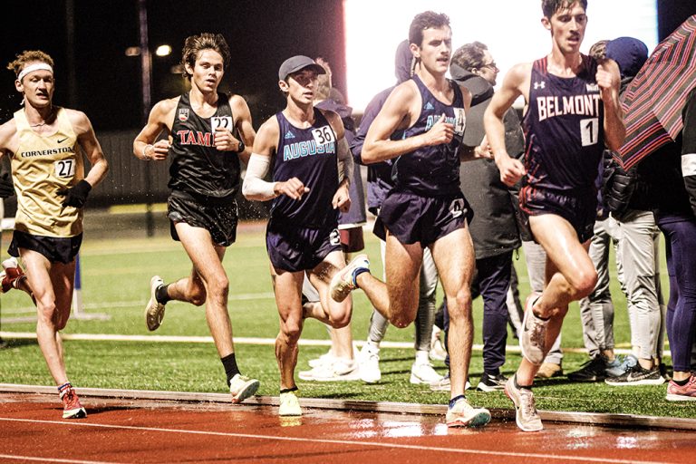 a group of 4 men run along the straightaway on the track